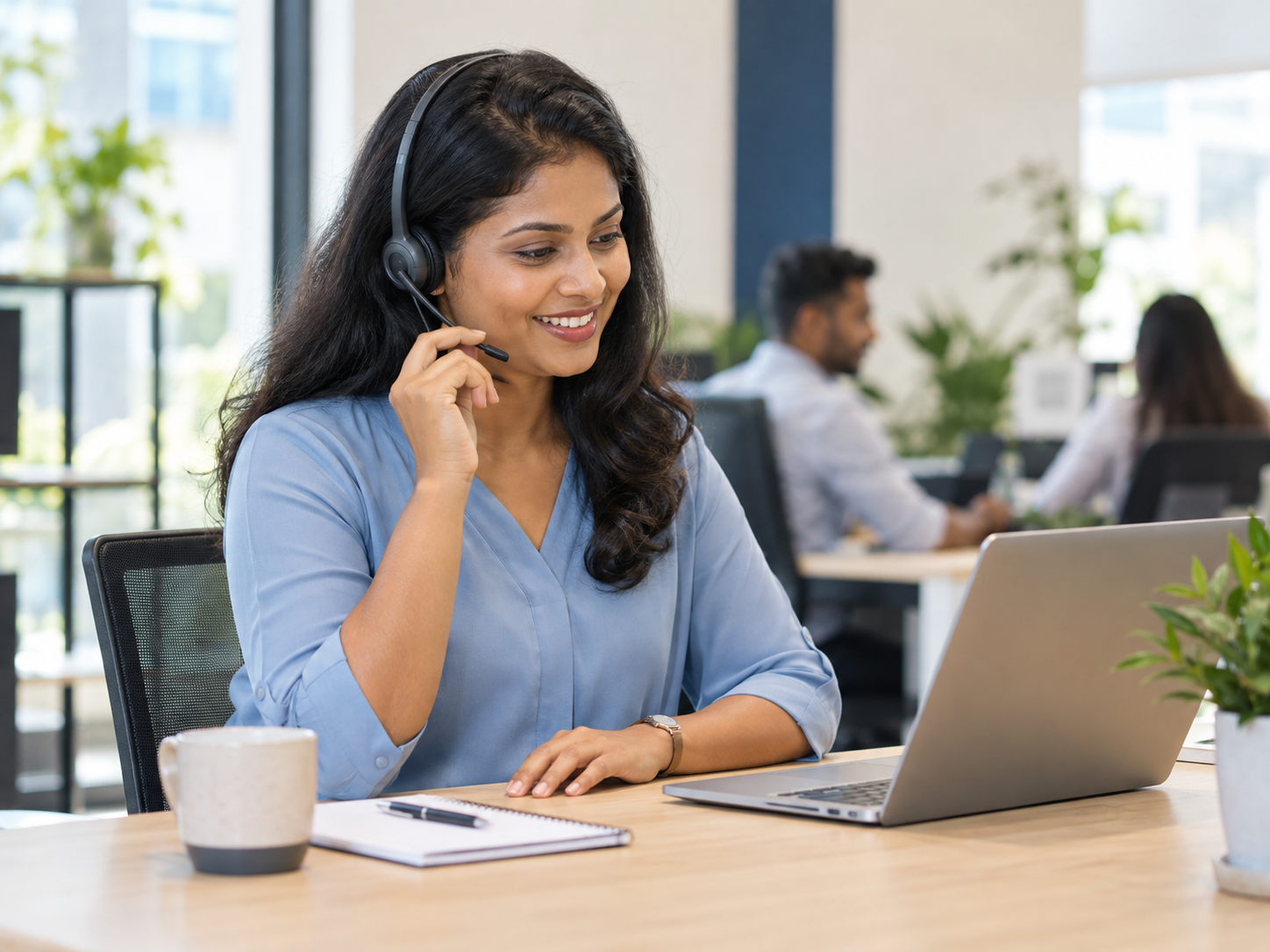 Support agent wearing a headset and helping a customer from her laptop in a bright office.